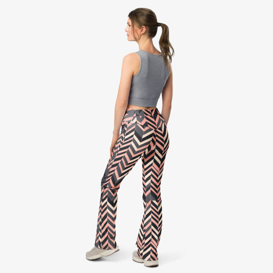 Woman wearing blush stripe flare leggings with a high waist and chevron pattern, posing with her back turned and hands relaxed, styled with a cropped grey tank top and sneakers.