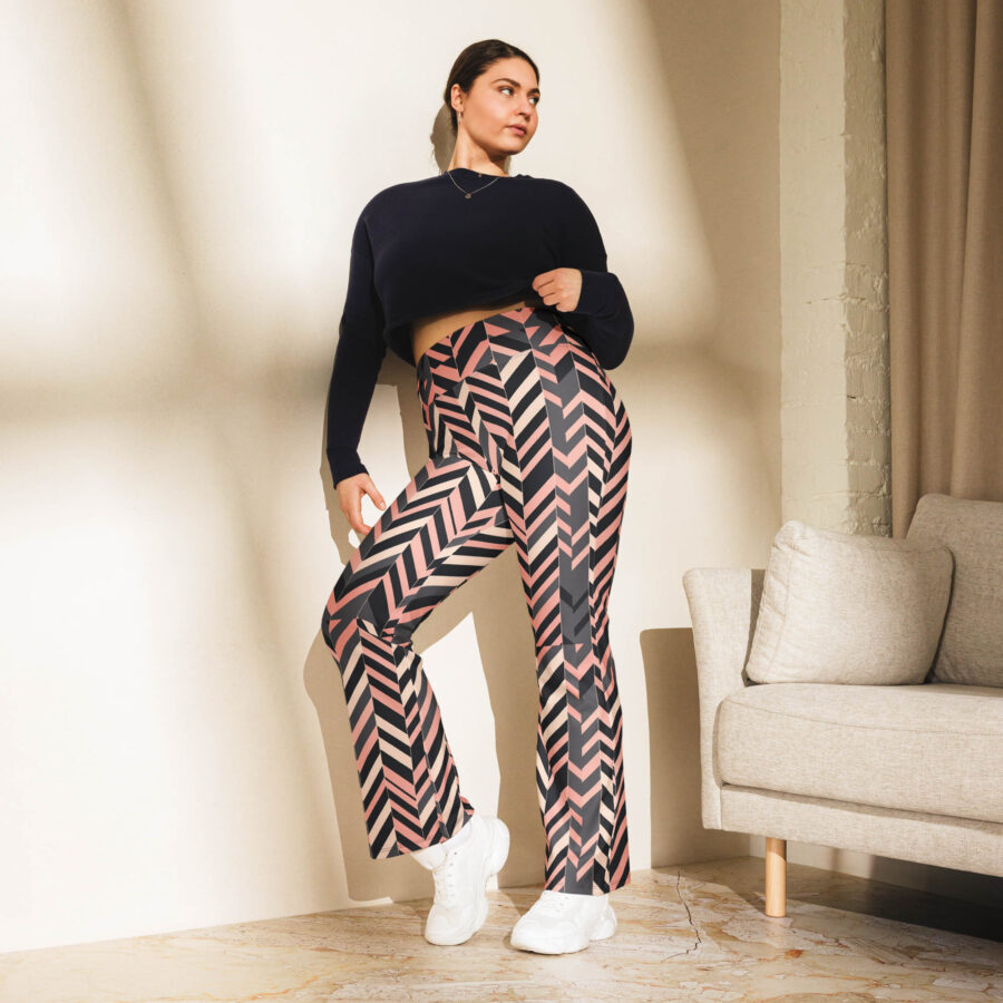 Confident woman posing in sunlight by a beige couch, wearing blush stripe flare leggings with a navy crop sweatshirt and chunky white sneakers.