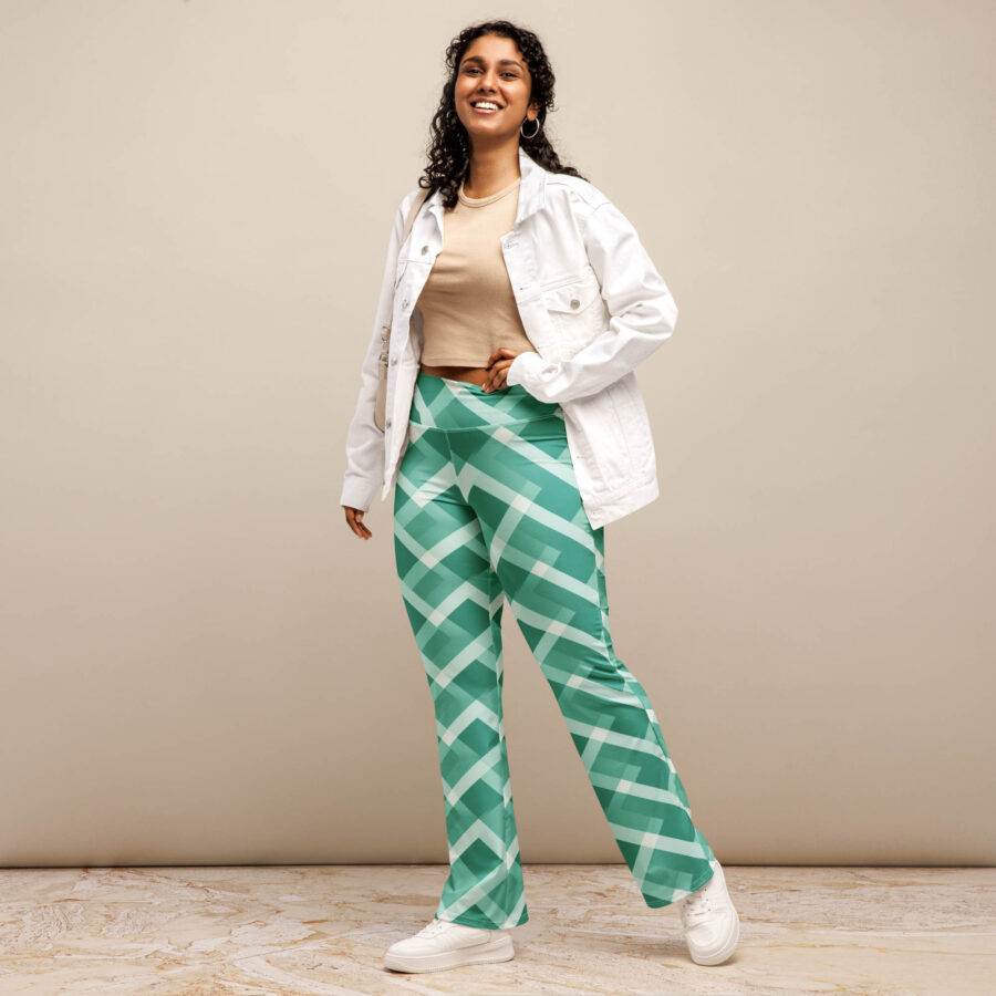 A smiling woman stands confidently in a beige top and white jacket, wearing emerald grid flare leggings with bold geometric lines.