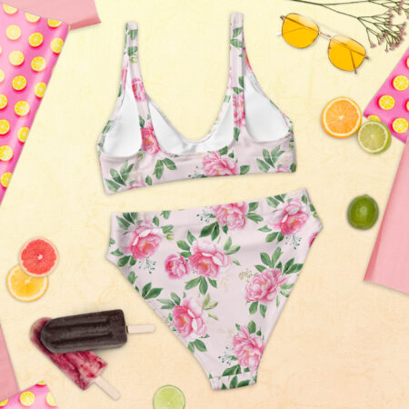 Floral Grace High Waisted Bikini laid flat on a summer-themed backdrop, showcasing the pink peony print on a soft pastel base.