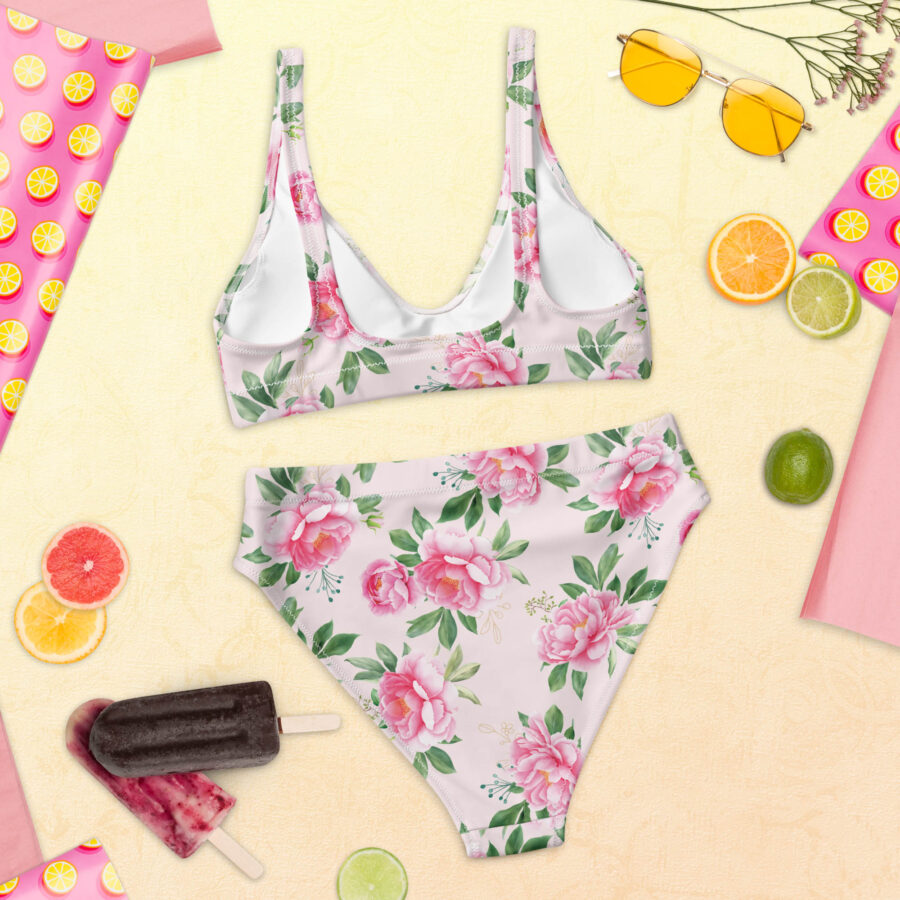 Floral Grace High Waisted Bikini laid flat on a summer-themed backdrop, showcasing the pink peony print on a soft pastel base.