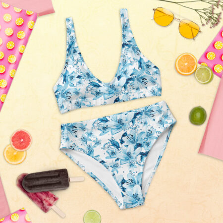 Flat lay of the Azure Bloom High Waisted Bikini set placed on a summery background with citrus fruits, flowers, and popsicles, highlighting the detailed blue floral design.