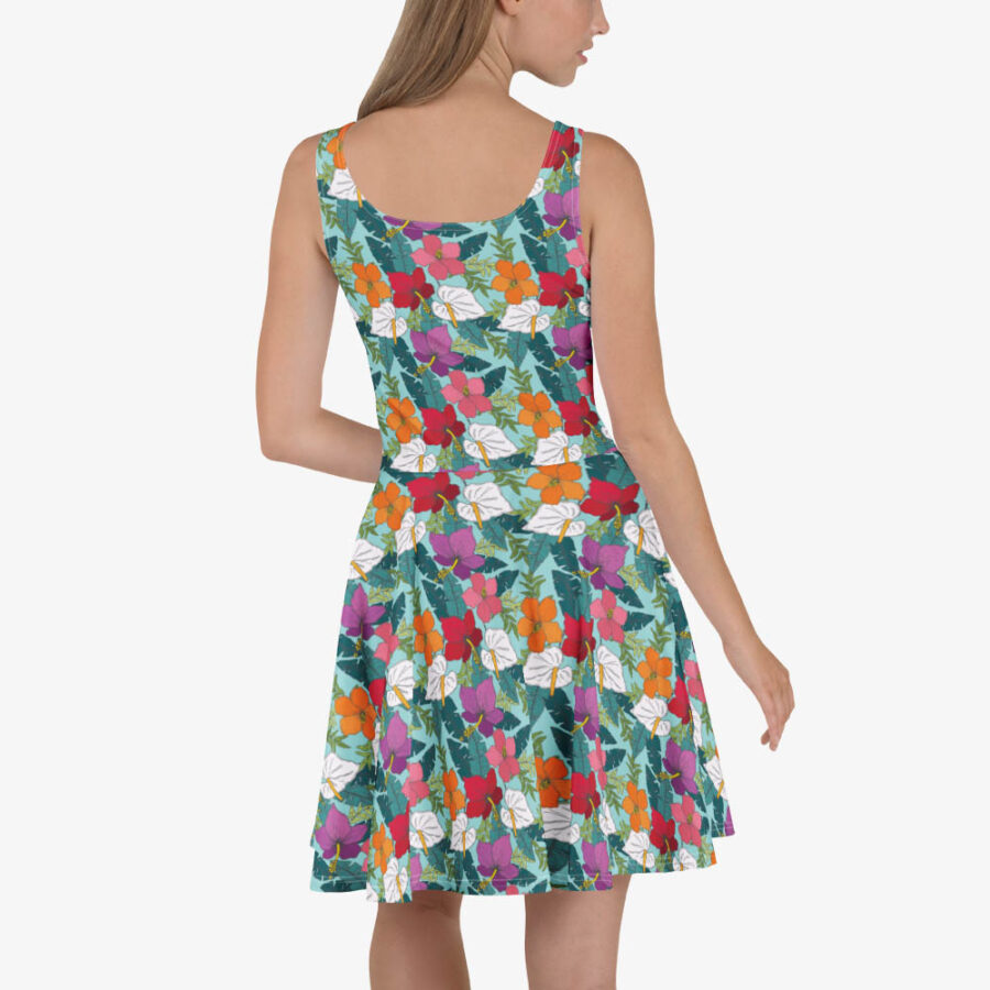 Woman wearing a vibrant floral skater dress with a scoop back, showcasing red, orange, purple, and white tropical flowers on a teal background.