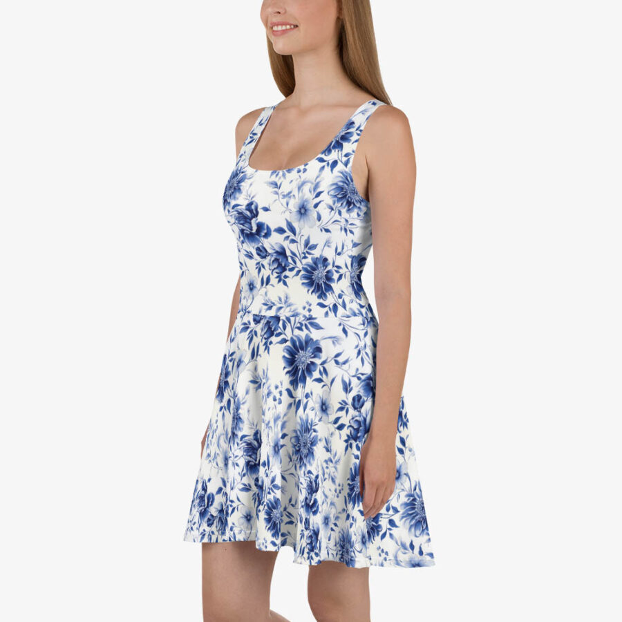Smiling woman modeling a white sleeveless skater dress with blue floral pattern, hands in side pockets.