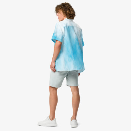 Man wearing a sky blue and white cloud-patterned short sleeve button shirt, viewed from the back, paired with pale shorts and white sneakers.
